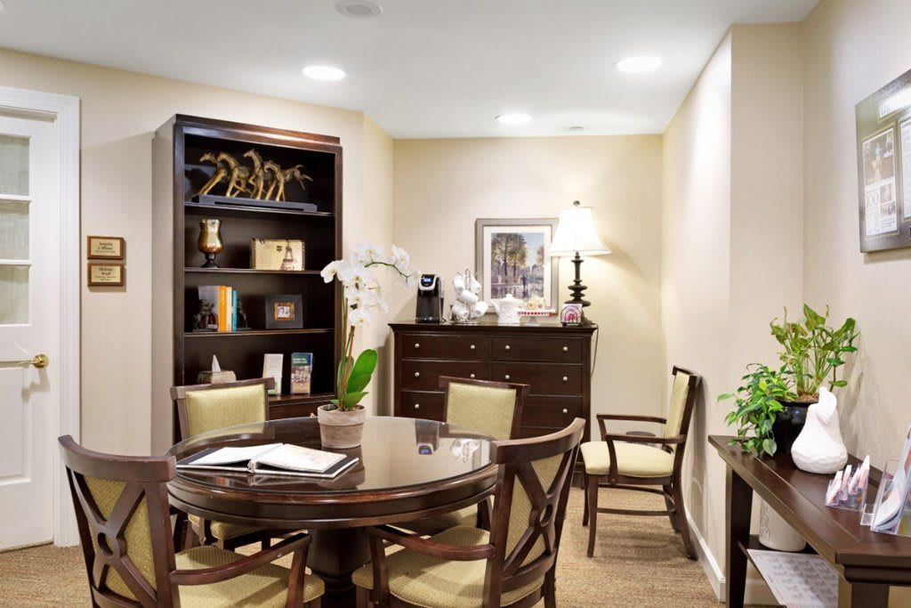 A well-furnished office space featuring a round table, chairs, a bookshelf, and decorative plants.