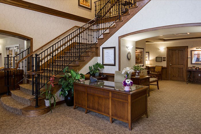 A welcoming office reception area featuring a wooden desk, lush plants, and a staircase.