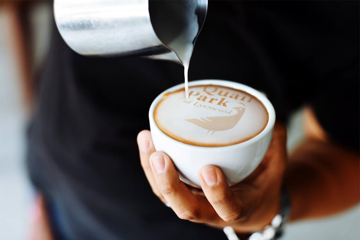 A barista skillfully pours milk into a cup of coffee, creating intricate latte art.