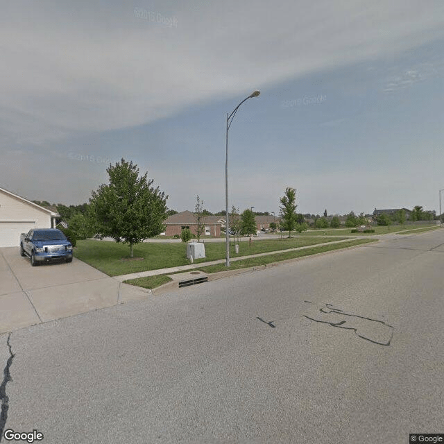 A suburban street view showing a residential neighborhood with houses, a car parked in a driveway, and a lamp post along the sidewalk.