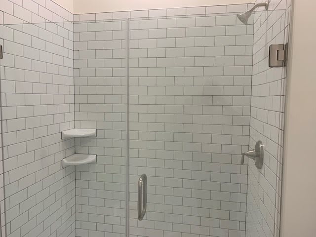 A modern bathroom shower with white subway tiles and a glass door.