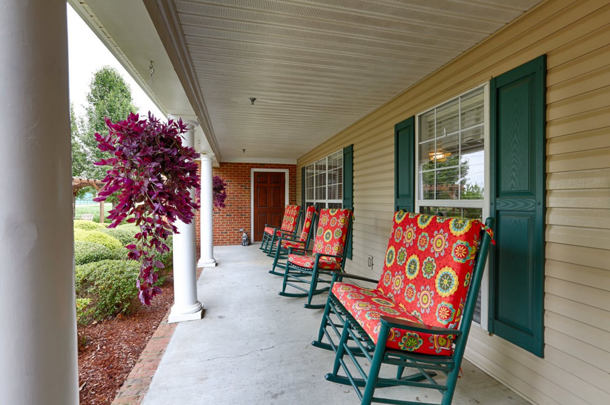 A cozy porch with colorful rocking chairs and lush greenery.