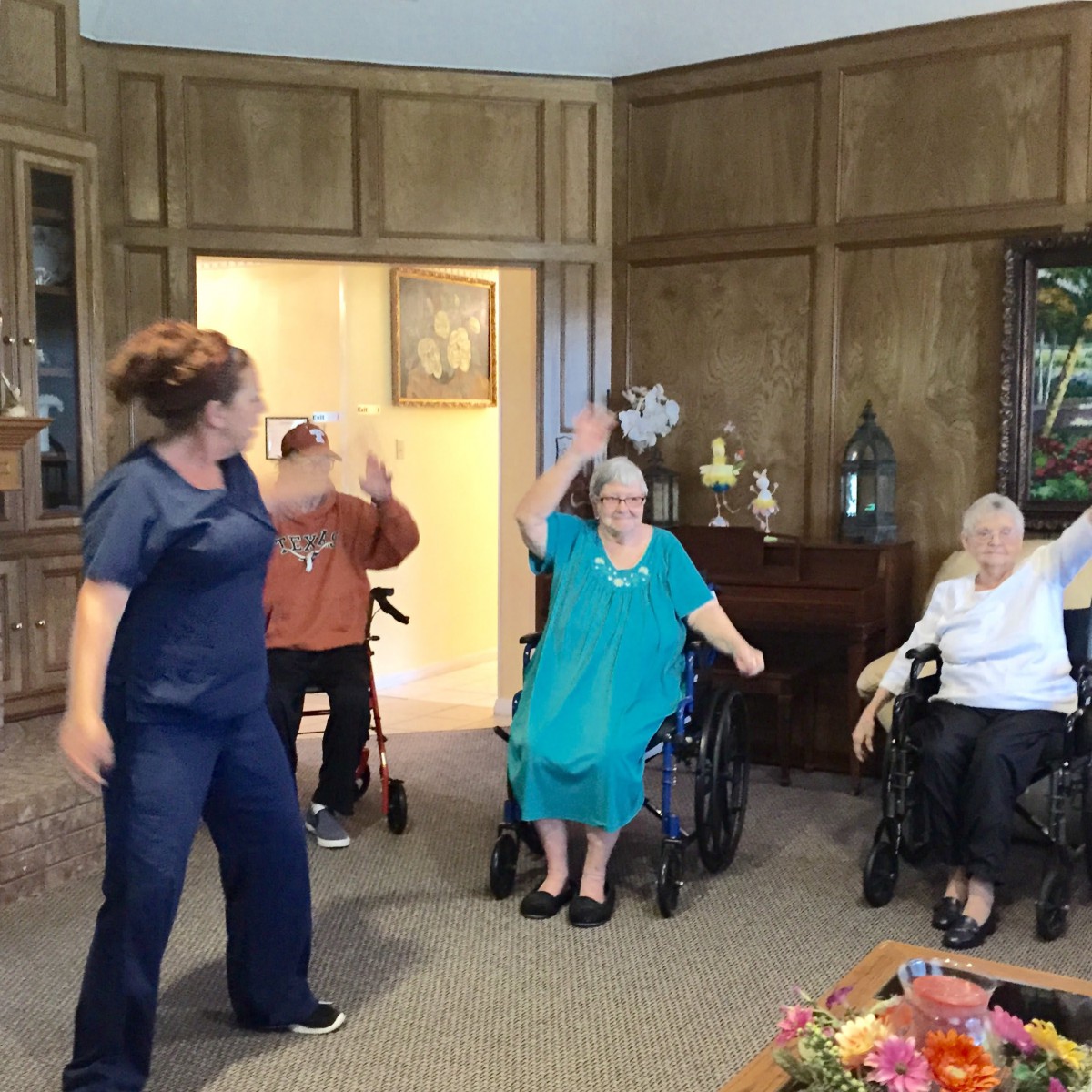 A caregiver leads a group of seniors in an exercise session inside a nursing home.