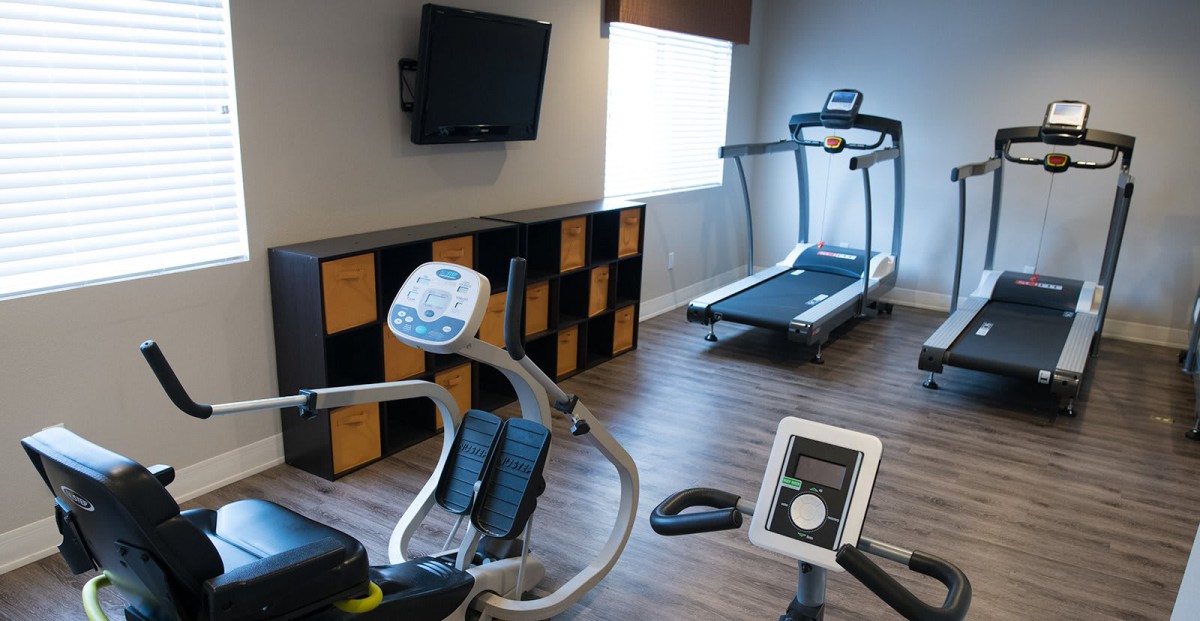 A modern gym with a treadmill, stationary bike, and a wall-mounted television.