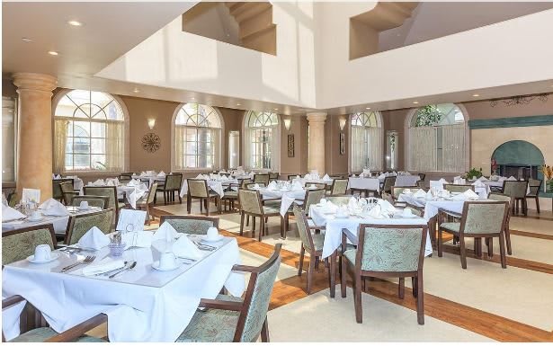 An elegant restaurant dining room with neatly arranged tables and chairs, featuring large windows and white tablecloths.