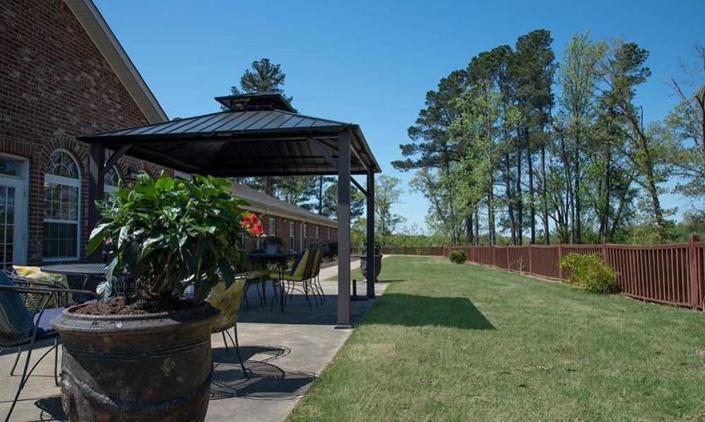 A backyard patio with a gazebo and outdoor furniture, overlooking a well-maintained lawn and trees under a clear blue sky.