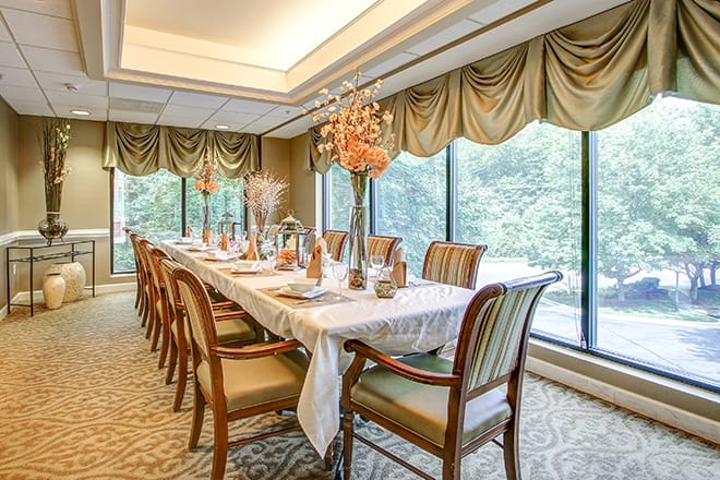 An elegant dining room set for a formal gathering, featuring a long table with luxurious chairs and a window view.