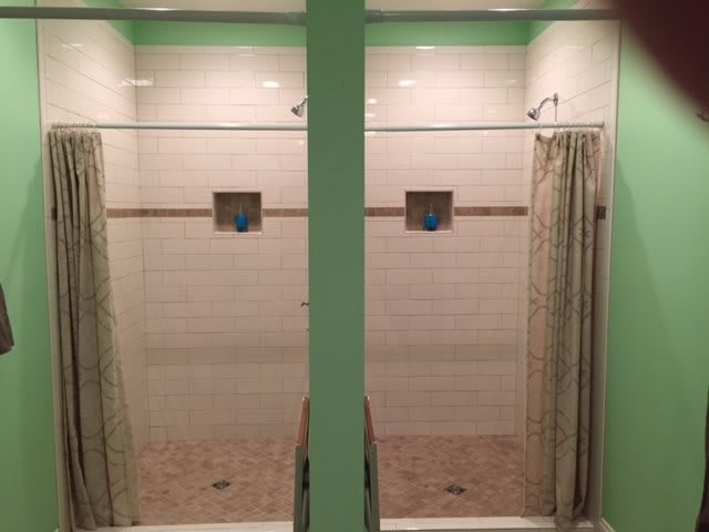 A bathroom featuring side-by-side tiled shower stalls with curtains.