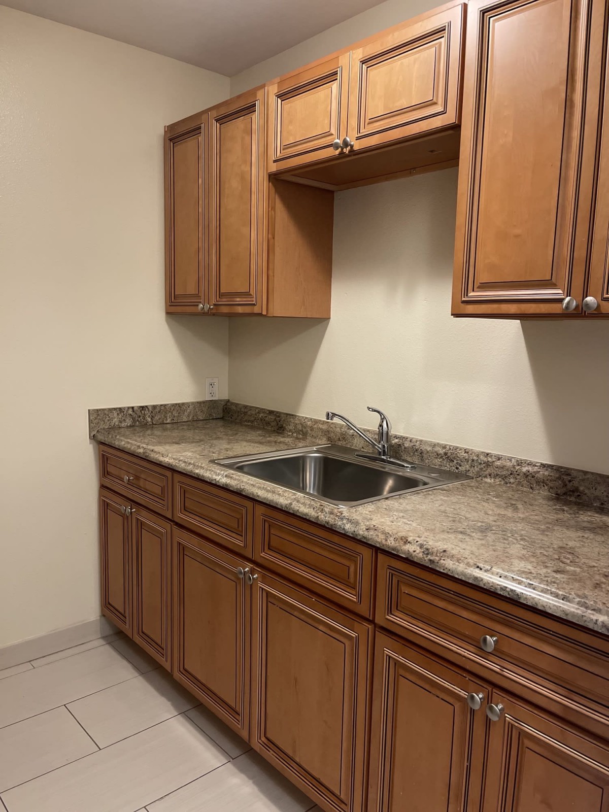 A kitchen featuring wooden cabinets and a marble countertop with a double sink.