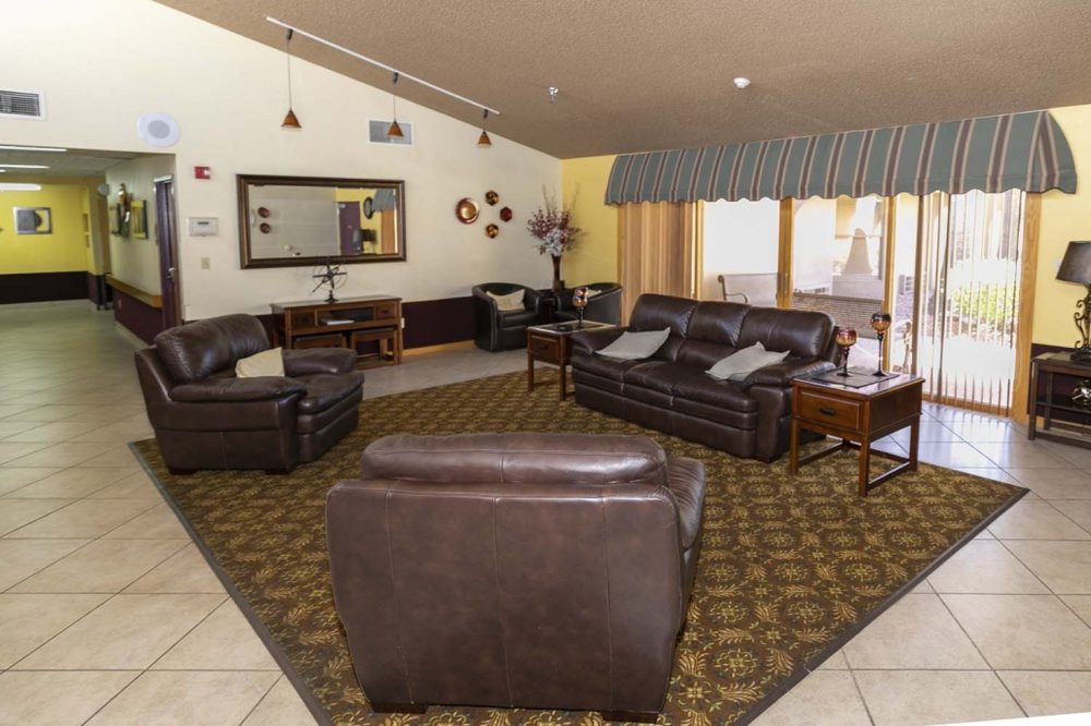 A cozy living room with dark leather sofas and an armchair, centered around a patterned carpet.
