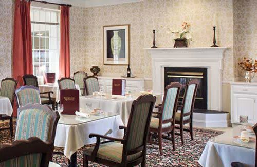 An elegant dining room with neatly arranged tables and chairs, featuring a fireplace and artwork on the wall.