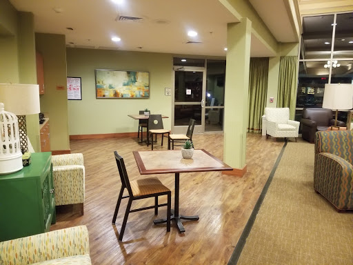 A cozy lobby area featuring tables and chairs, accented by green walls and warm lighting.