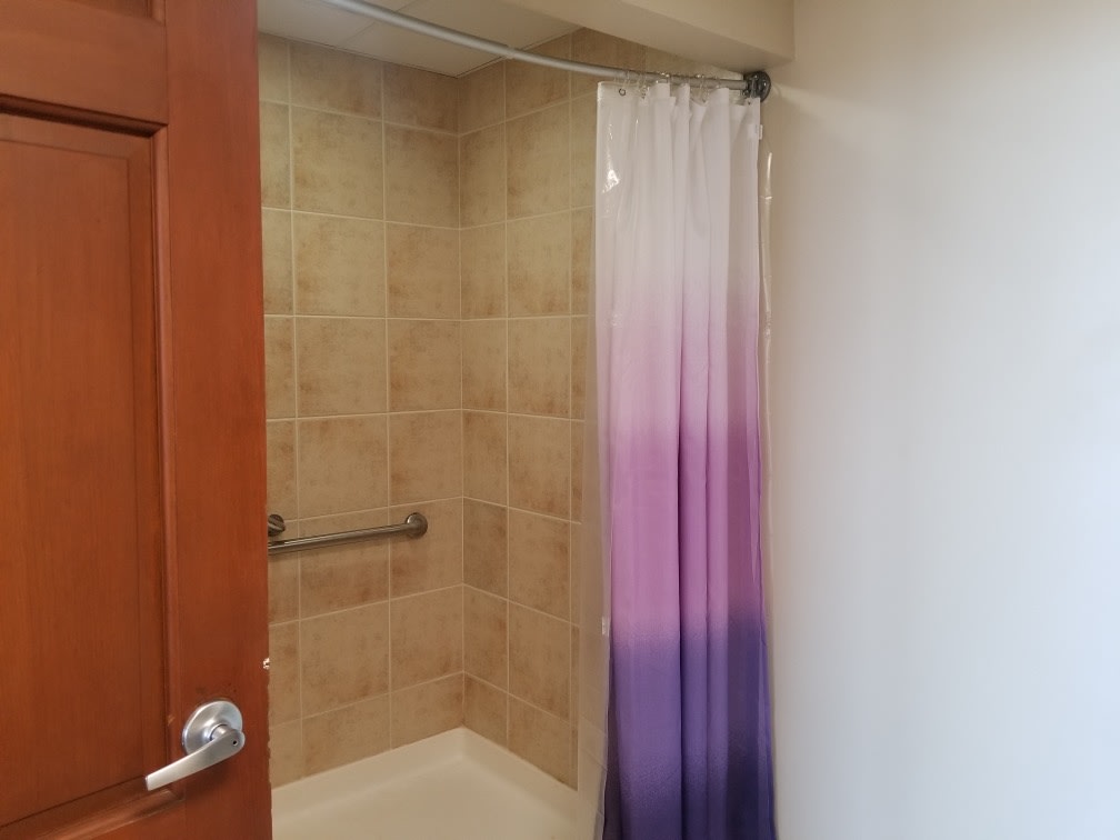 A bathroom with a tiled shower area featuring a purple gradient shower curtain and a grab bar.