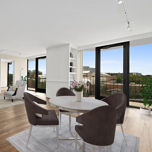A modern dining area featuring a round table and stylish chairs, illuminated by natural light streaming through large windows.