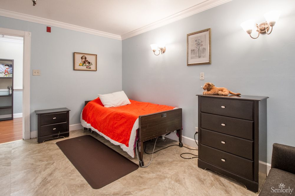 A cozy bedroom with a single bed featuring red bedding, a nightstand, and a dresser against light blue walls.