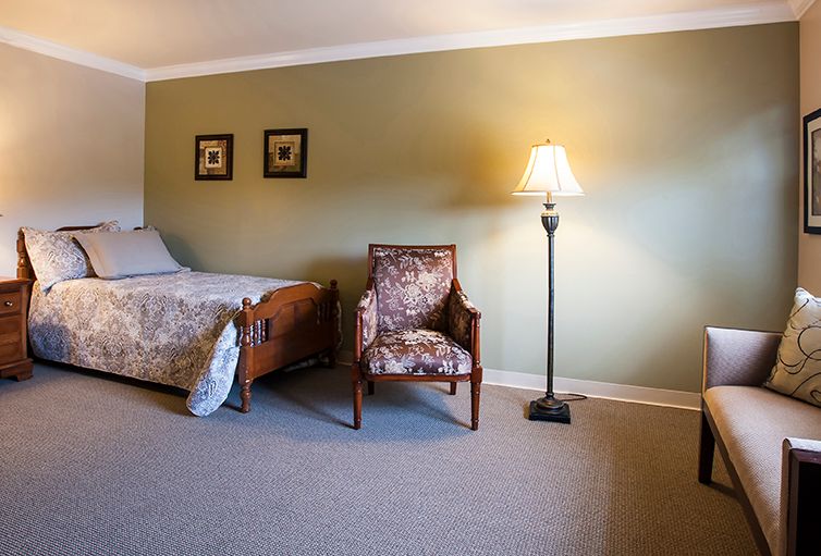 A cozy bedroom with a bed, an upholstered chair, and a floor lamp against a green accent wall.