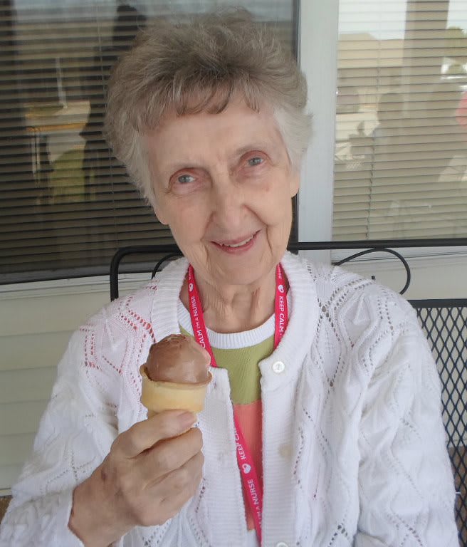 An elderly woman enjoys an ice cream cone while sitting outdoors.