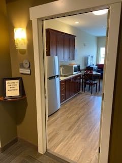 A view into a modern kitchen and dining area with wooden flooring, featuring a refrigerator and microwave.