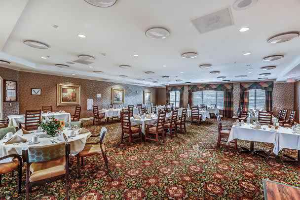 A spacious dining room with elegantly set tables and chairs on a patterned carpet.