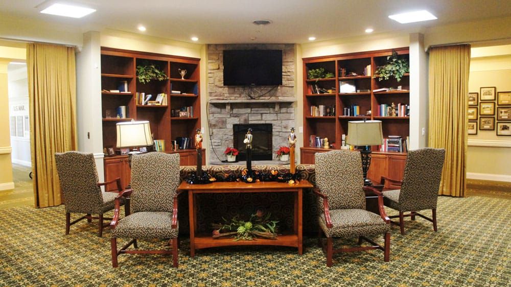 A cozy library with a fireplace, surrounded by bookshelves and comfortable seating.
