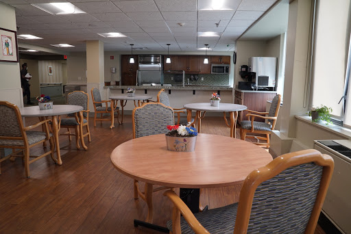 A spacious dining area featuring wooden tables and chairs, with a kitchenette in the background.