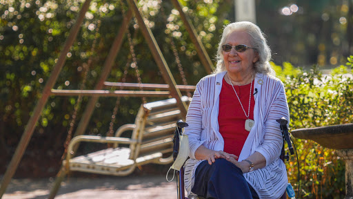 An elderly woman enjoys a sunny day, smiling while seated near a swing.
