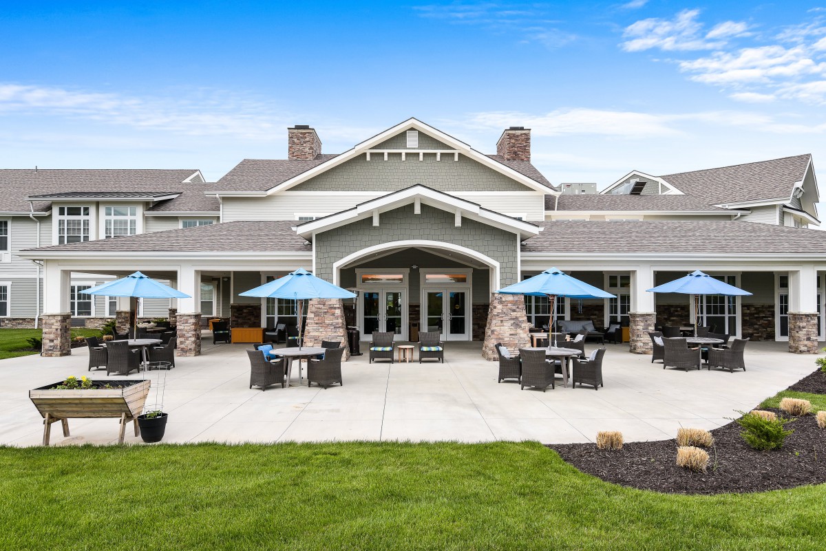 A stylish restaurant building with outdoor seating and blue umbrellas under a clear blue sky.