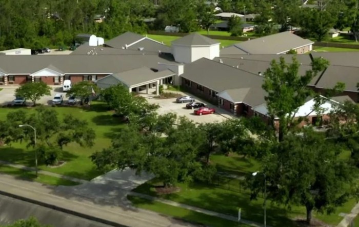 Aerial view of a building surrounded by trees and a parking lot in a residential area.