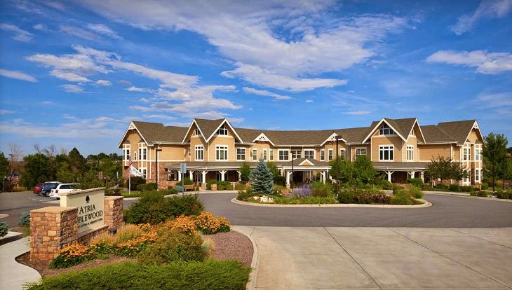 A large residential building surrounded by landscaped gardens under a blue sky with clouds.