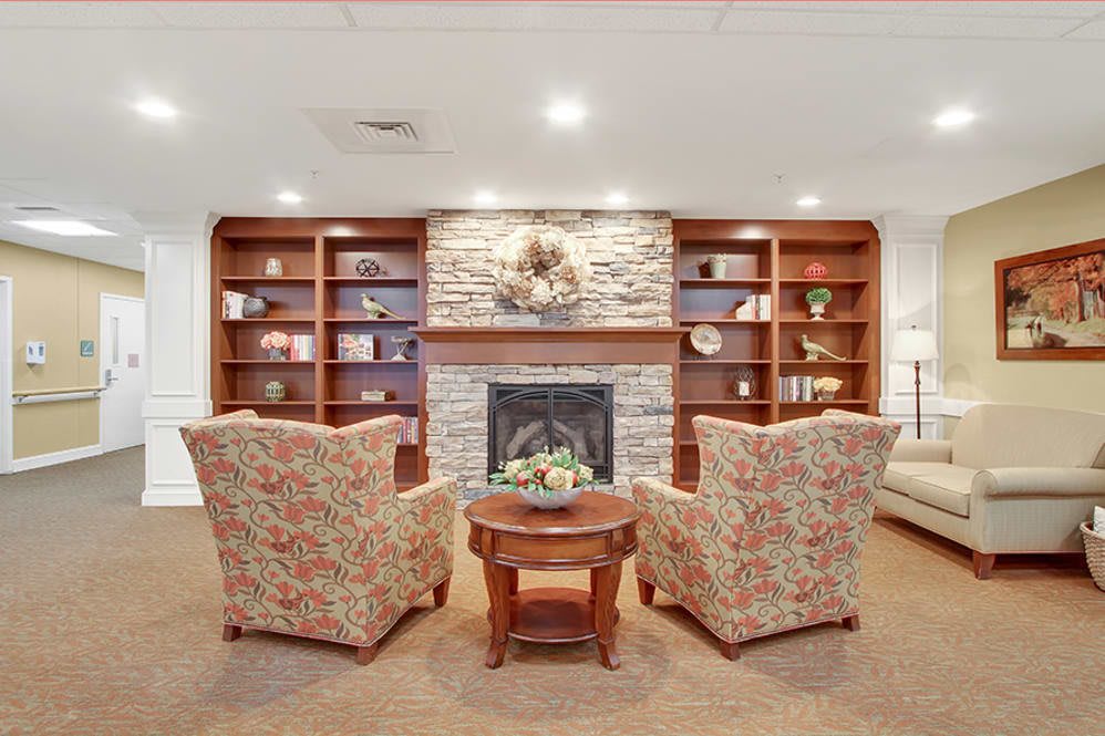 A cozy living room with armchairs facing a fireplace flanked by wooden bookshelves.