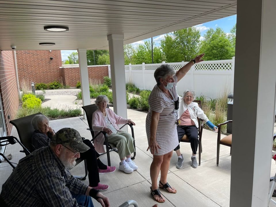A group of seniors enjoying an outdoor activity on a patio, led by a person pointing at something in the distance.