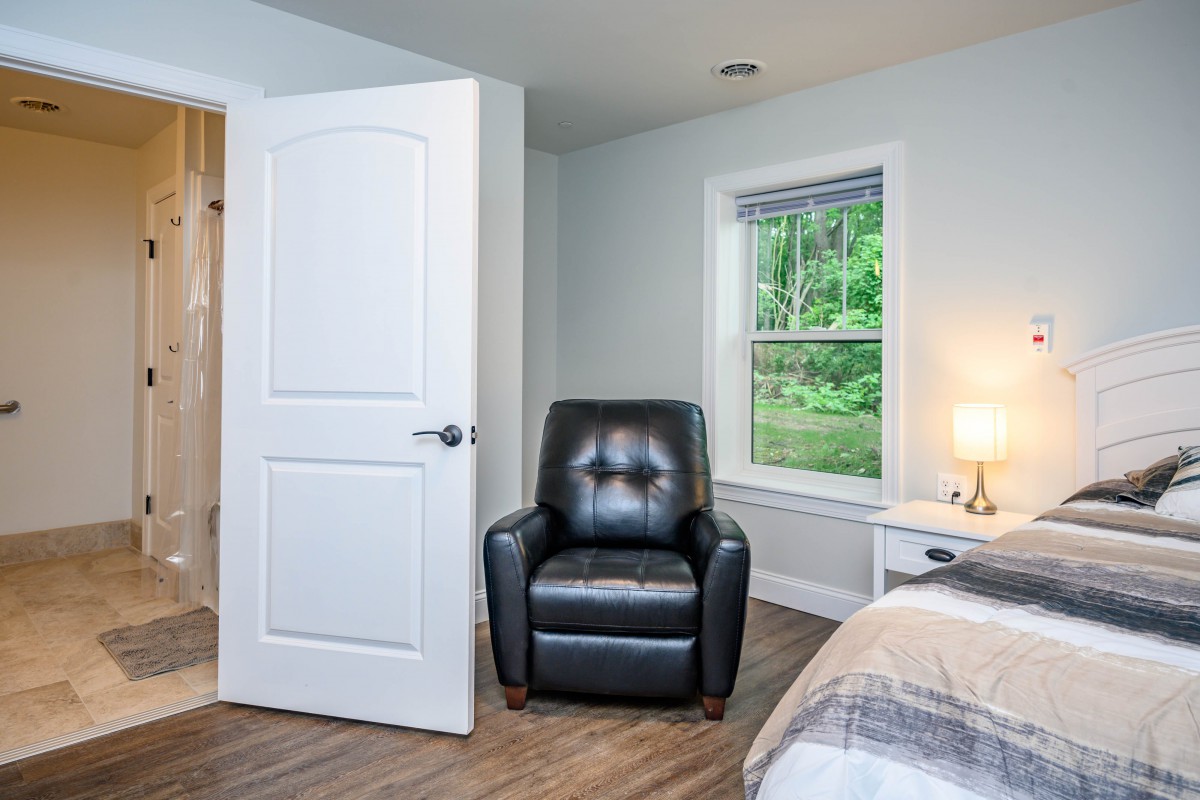 A cozy bedroom with a leather chair, bedside lamp, and open window.