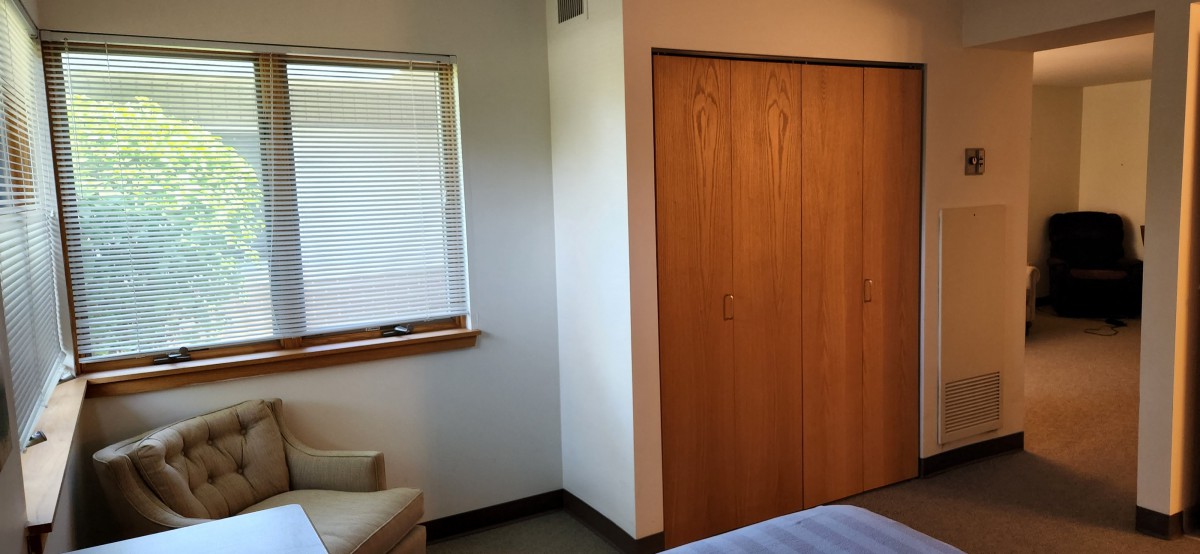 A minimalist bedroom with a wooden closet and window featuring closed blinds.