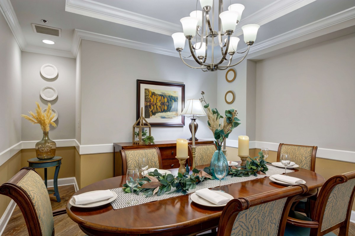 A beautifully set dining room table with elegant decor, featuring a chandelier and decorative elements such as candles and a painting.