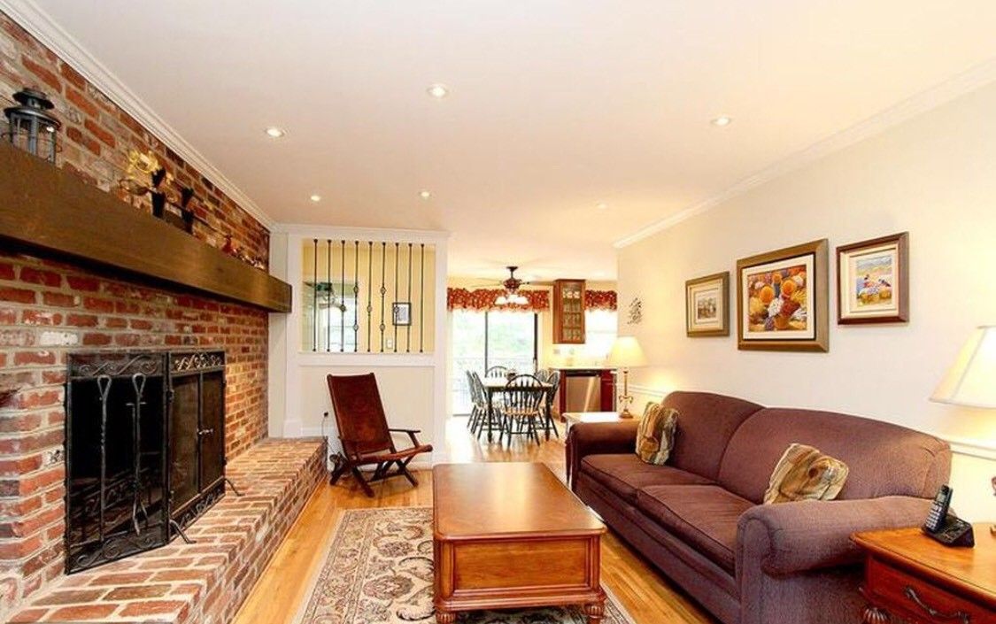 A cozy living room with a brick fireplace, comfortable sofa, and a view of the dining area.