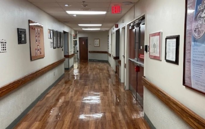 A clean and polished hospital hallway with several doors and framed pictures on the walls.