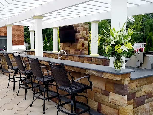 A stylish outdoor bar area featuring a stone countertop, high chairs, and a beautiful floral arrangement.
