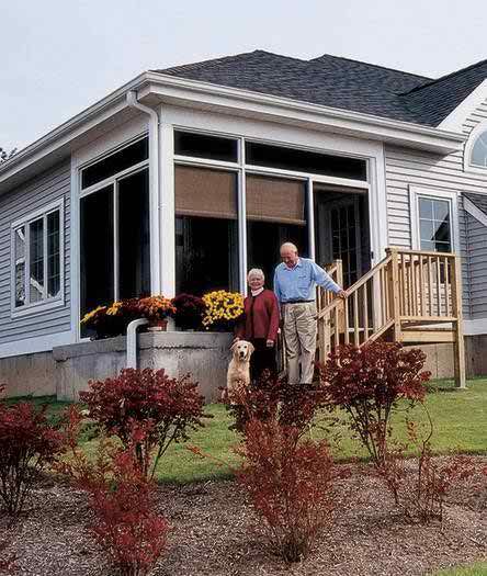 An elderly couple with their dog standing on the porch of their house, surrounded by a well-maintained garden.