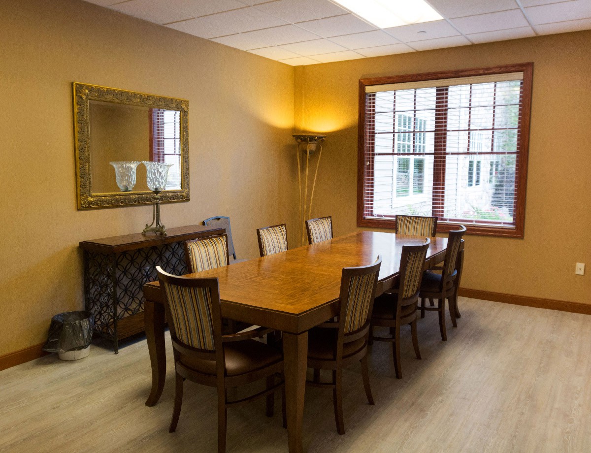 A well-furnished conference room with a large meeting table and chairs, featuring a mirror and window.