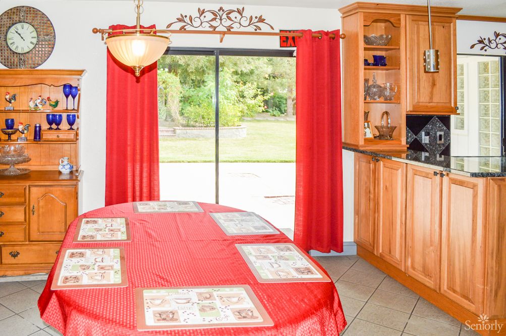 A cozy kitchen dining area with red curtains and wooden cabinets.