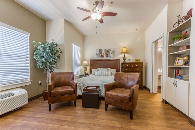 A cozy bedroom with two leather chairs, a bed, and wooden flooring.