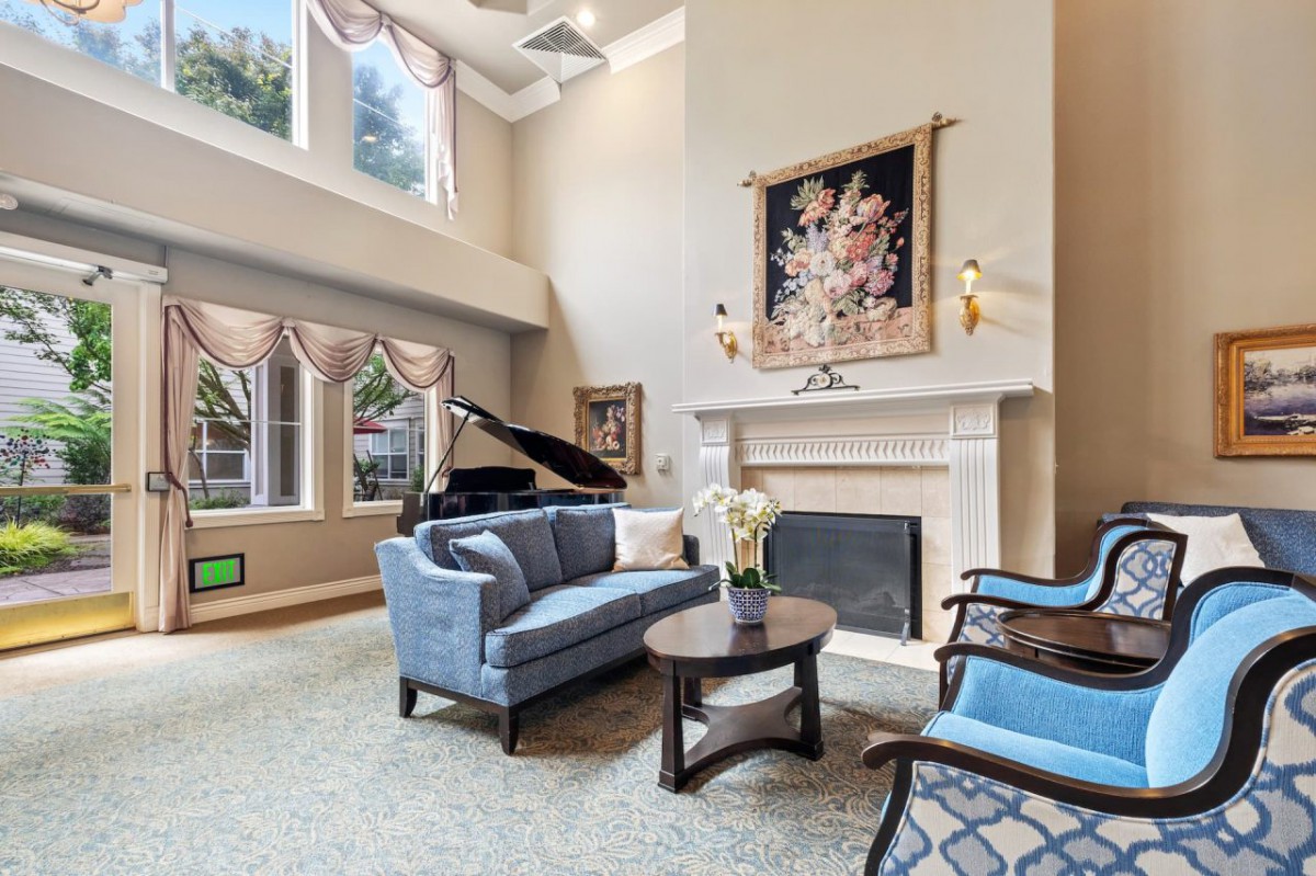 A spacious living room featuring a grand piano, elegant furniture, and a warm fireplace with artwork above.