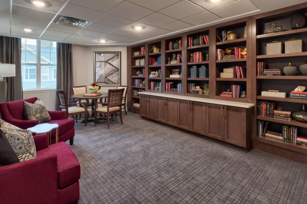 A cozy library room with bookshelves, a table and chairs, and art on the wall.