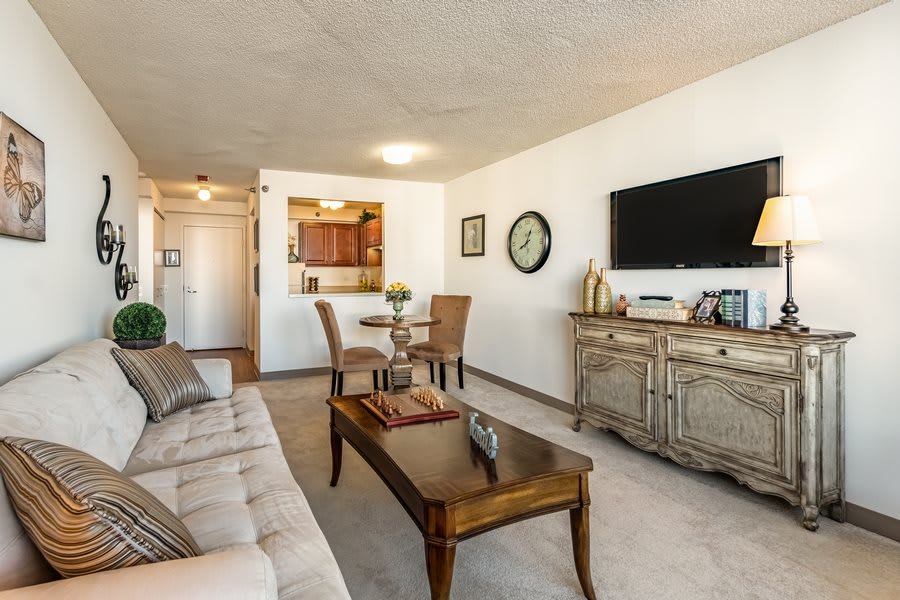 A modern living room with a comfortable sofa, wooden coffee table, and a wall-mounted television, adjacent to a small dining area.