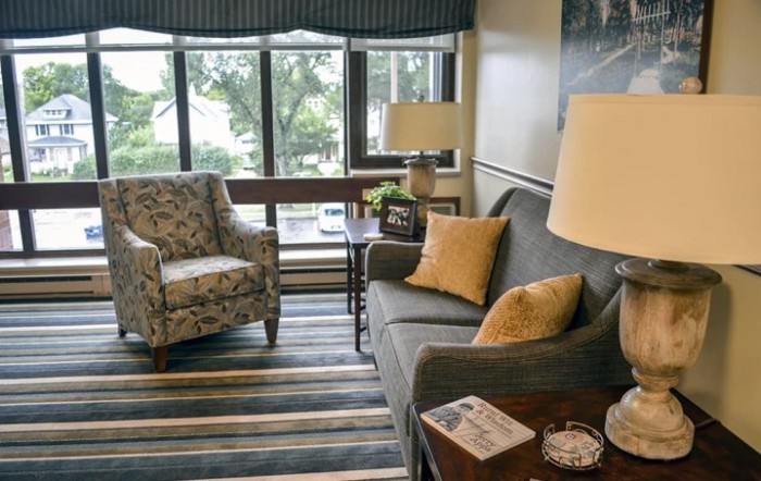 A cozy living room with a sofa, armchair, and large window, featuring a striped rug and tasteful decor.