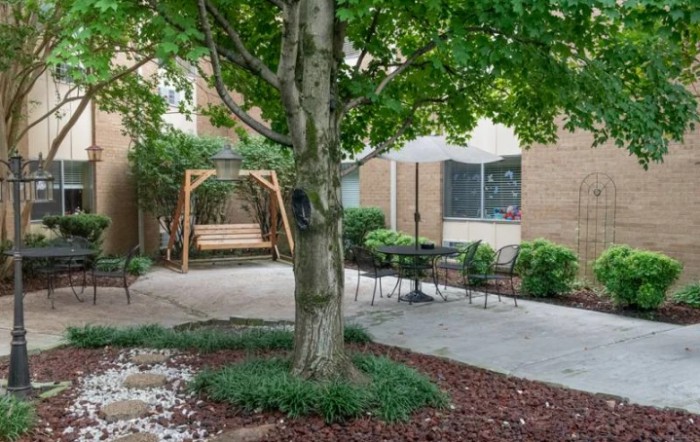 A peaceful garden with a tree, swing, and patio seating area.