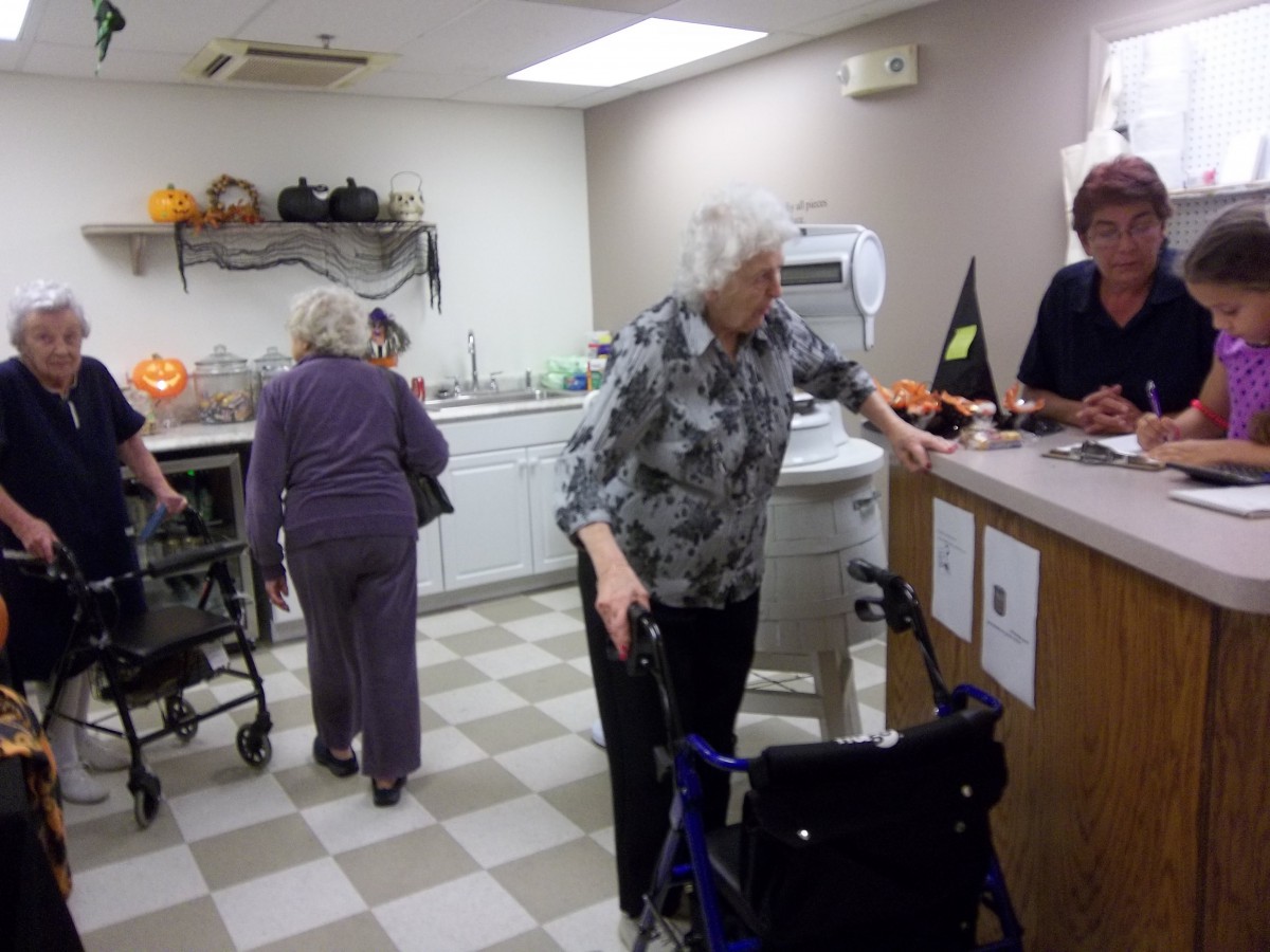 Elderly individuals interacting in a kitchen setting with assistance from staff.
