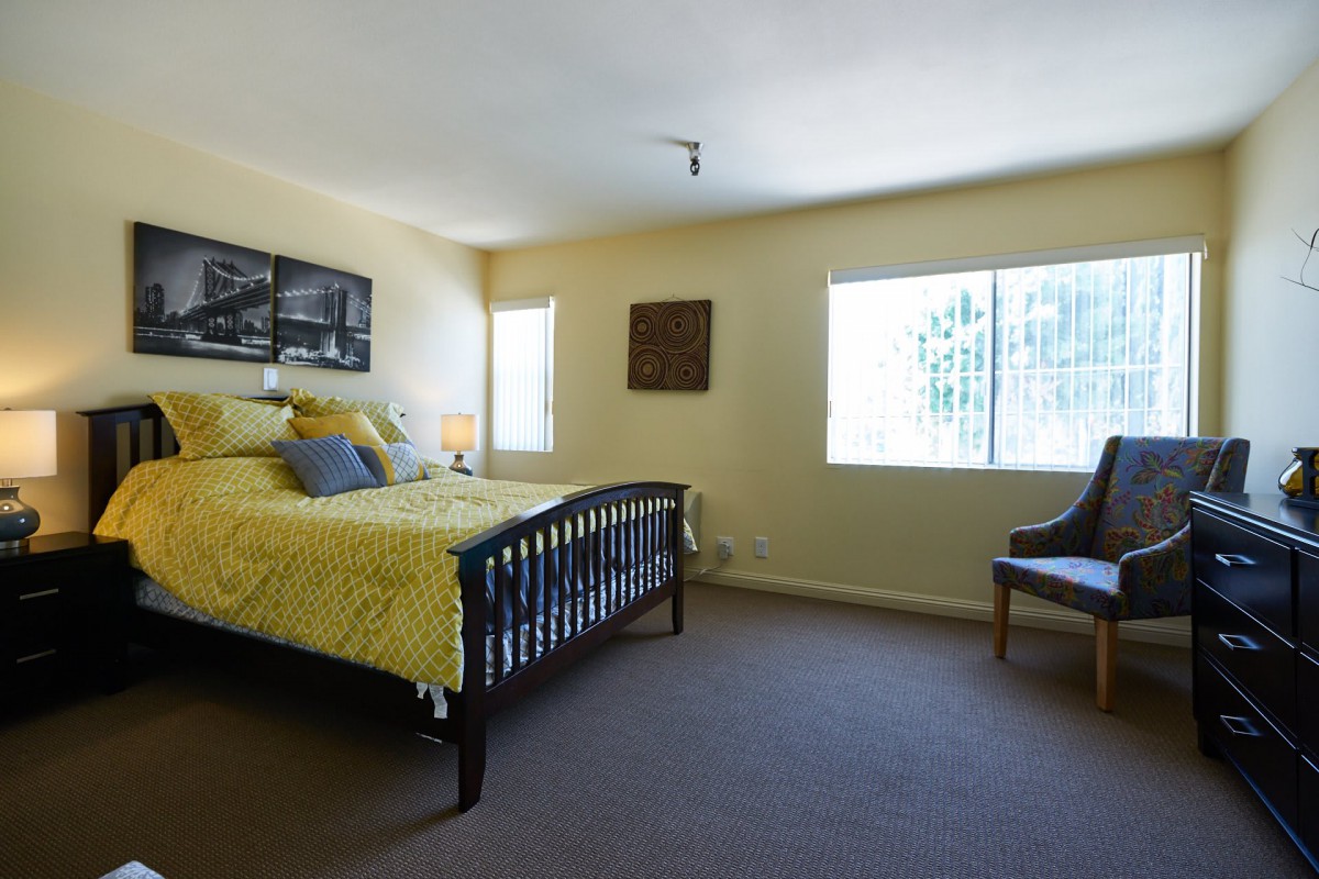 A cozy bedroom with a bed, chair, and windows allowing natural light.