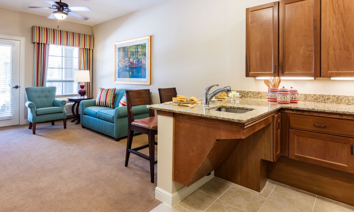A cozy living room with a kitchenette, featuring a sofa, bar stools, and modern decor.
