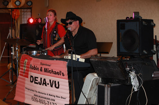 A live band performing at a venue, featuring a keyboard player in a black hat and another musician in the background.
